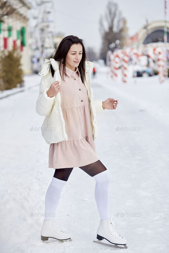 Stylish brunette girl ice skates outdoor in winter. Festive holidays mood. Dreams come true concept