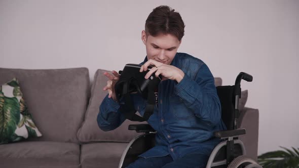 Disabled Young Man in Wheelchair Putting on VR Goggles. Guy Teenager Holding Virtual Reality Glasses