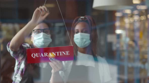 Two Waiters in Masks Hanging Quarantine Sign on Restaurant Glass Door Closing Place alt