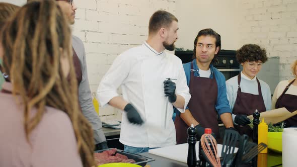 Handsome Man Chef Sharpening Knife Teaching Cooking Class Students Indoors alt