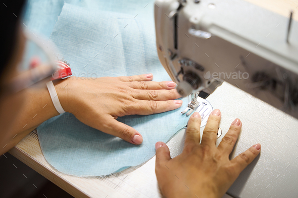 Professional dressmaker woman sews clothes on sewing machine at