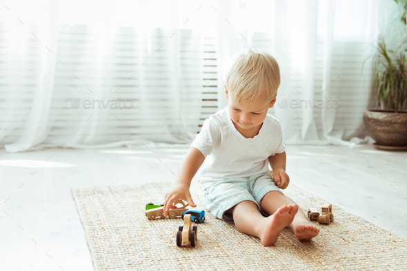 Child boy playing with wooden cars toys, sitting on the floor, while staying at home, eco minimalism