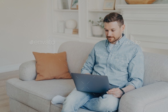 Man in casual wear focused on his laptop, comfortably working from home on a cozy couch