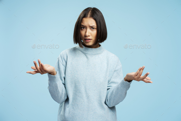 Serious young asian woman holding hands to sides, not understanding something, looking at camera