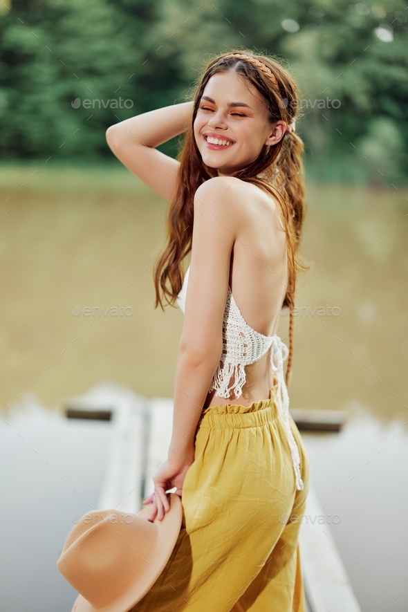 A young woman smiling in an image of a hippie and eco-dress dancing in nature by the lake wearing a