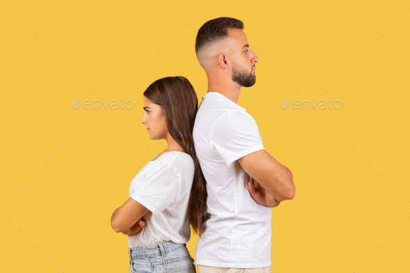 Sad angry millennial european wife and husband in white t-shirts back to back, ignoring after