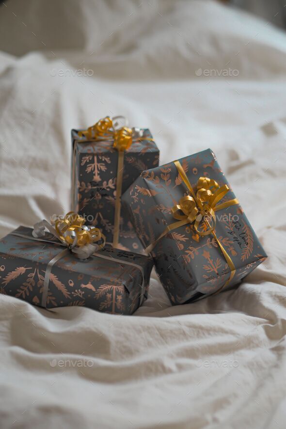 three wrapped presents are on the bed on a sheet with a bow Stock