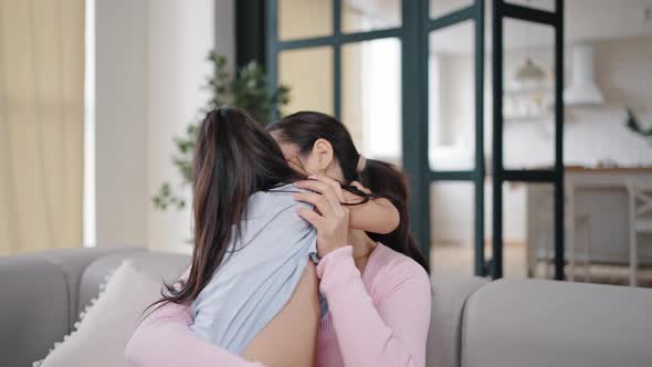 Happy Brunette Mother Hugs Running Daughter Sitting on Couch alt