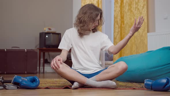 Portrait of Positive Young Caucasian Man Examining Biceps Sitting in Retro Home alt