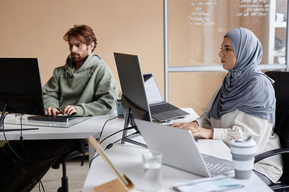 Middle Eastern Woman Working with Multiple Computers in IT Development Studio