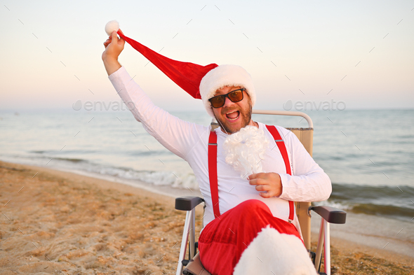 Santa in red suspenders against the background of the sea and the beach pulls off an artificial