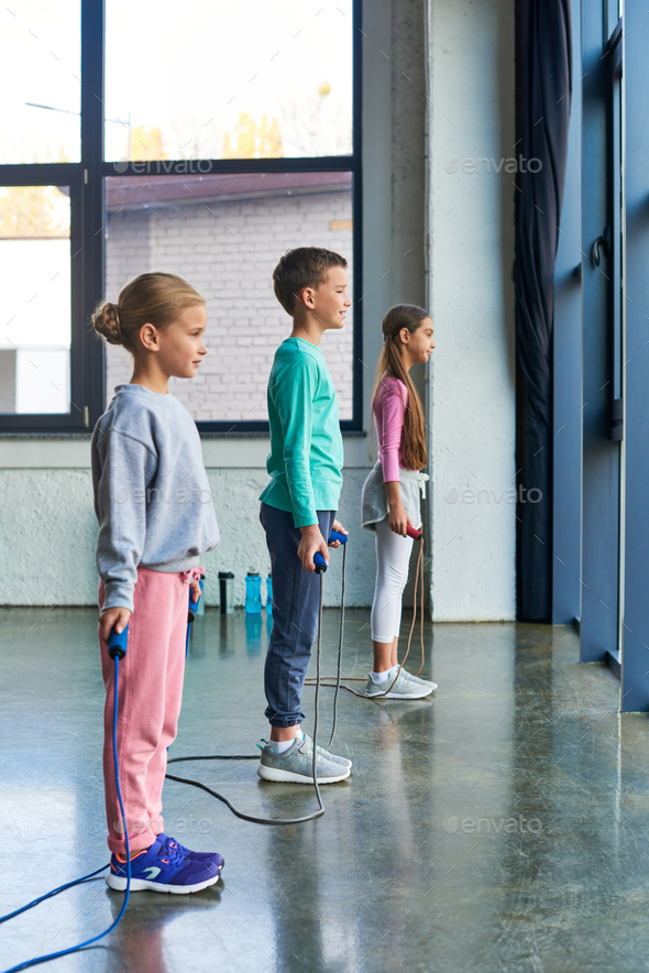 vertical shot of little cute girls and boy posing with jump rope and looking in front of them, sport