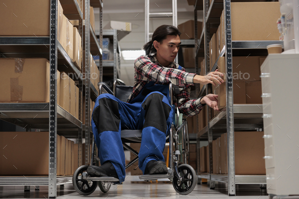 Warehouse asian package handler in wheelchair searching cardboard box