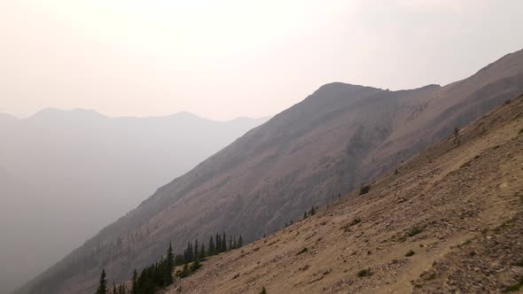 Drone flying backwards revealing a mountainside scenery ravaged by wildfires. Smoke covering the nat alt