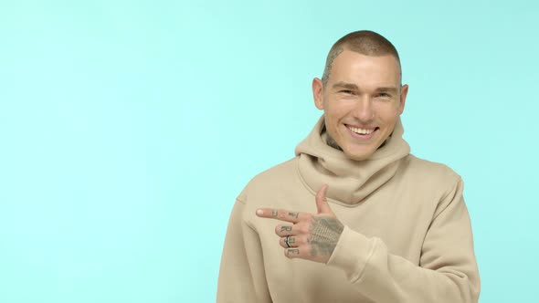 Cool Tattooed Guy in Trendy Hoodie Pointing Finger Left and Smiling Nod in Approval Recommending