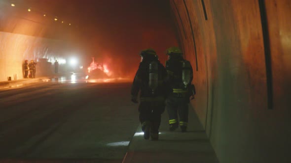 Firefighters inside a dark tunnel with emergency lights in the background alt