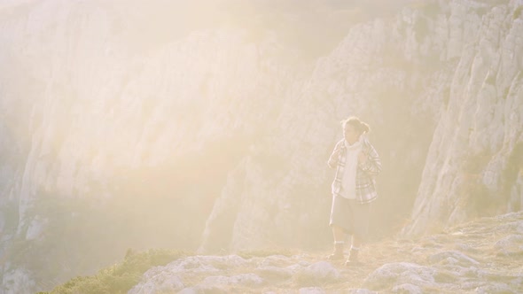 Woman with Backpack Walks Along Rocky Hill Against Mountains