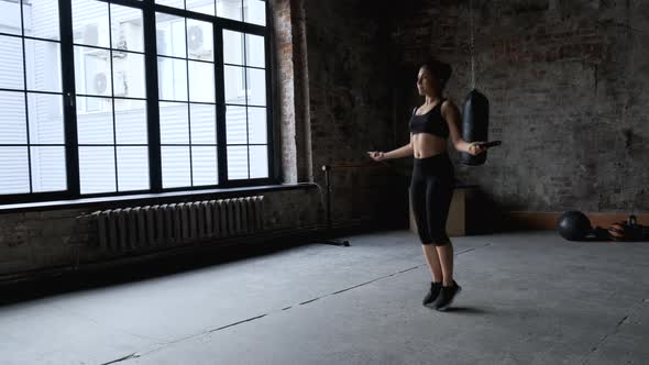 Young indian woman skipping rope in dark gym, Athletic Girl Dressed in Sportswear Black Top alt
