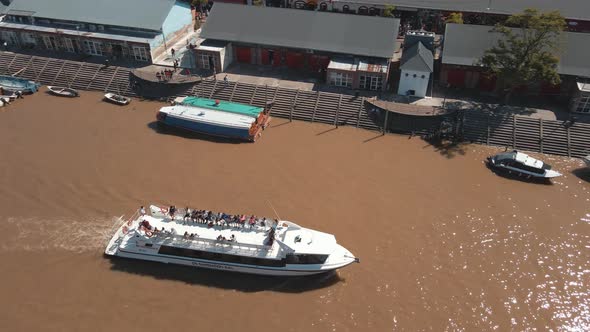 Catamaran sailing through a waterway with some people aboard at Tigre, Buenos Aires alt