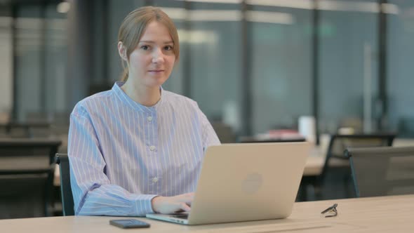 Young Woman Showing Thumbs Up Sign While Using Laptop in Office alt