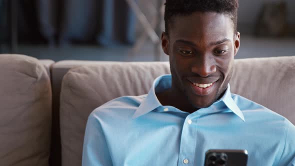 Smiling young male sending messages using smartphone on the couch alt