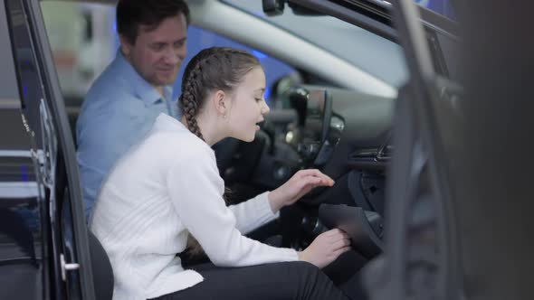 Side View of Girl Opening Glove Compartment and Taking Candy with Blurred Man Talking at Background alt