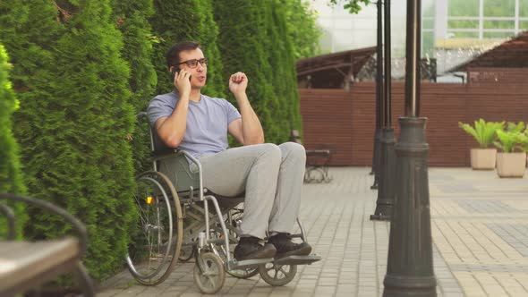 Attractive Disabled Guy in a Wheelchair Talking on the Phone and Smiling alt