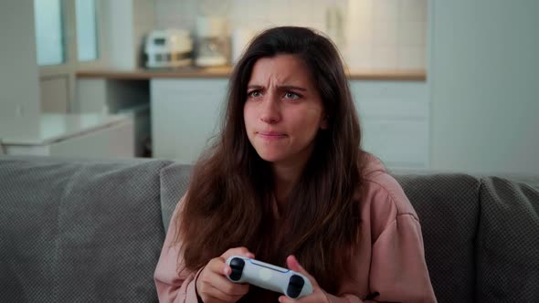 a Girl at Home Sits on the Couch and Plays a Console on a White Cordless Joystick