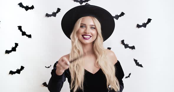 Hocus Pocus. Cheerful Halloween Witch Gesturing with Magic Wand at Camera, Making Miracle alt