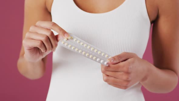 Video of biracial woman holding yellow tablets on pink background alt