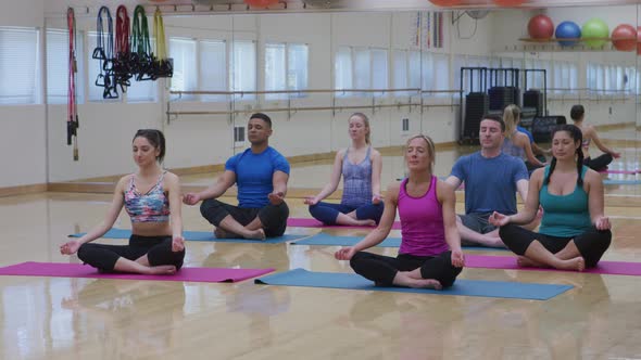 Group of men and women sitting on floor doing yoga at studio
