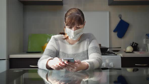 Woman in Medical Mask Reads Information on the Phone at Home, Takes Off the Mask, End of the