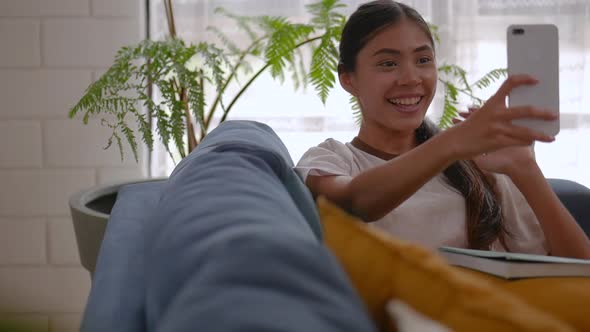 Young Asian woman using smartphone video chatting while sitting on a sofa.