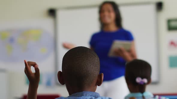 African american boy sitting in classroom raising hand to answer questions during lesson alt