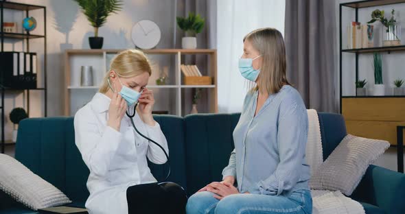 Doctor in Protective Mask Checking Heart and Lungs in sick 50-aged Woman During Home Visit alt