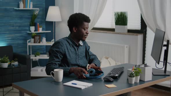 Freelancer of African Ethnicity Putting Headphones on While Working From Home alt