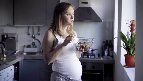 Cheerful Pregnant Woman Eating Salad and Rubbing Belly alt