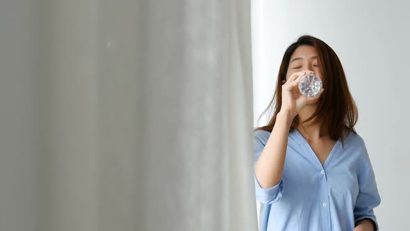 Beautiful young woman Asian drinking water Beside the window at home.