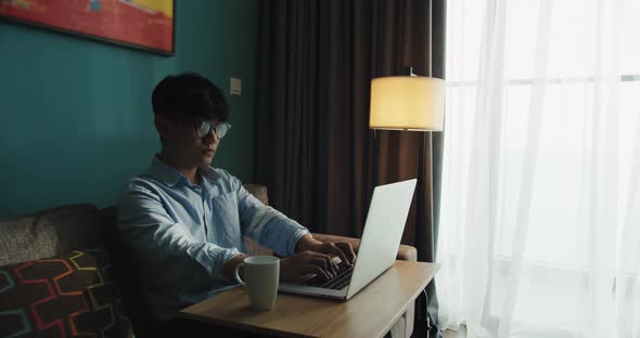 Young Attractive Asian Vietnam Man Busy Work Computer or Smart Tablet on Laptop at Home in Freelance alt