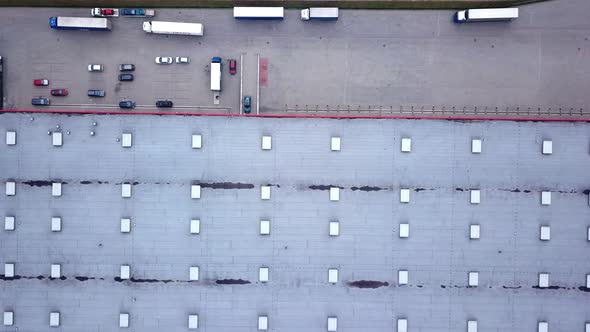 Moving Aerial Side Shot of Industrial Warehouse Loading Dock where Many Truck with Semi Trailers Loa alt