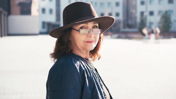 Portrait of a Senior Woman in Glasses and a Hat Looking to the Camera alt