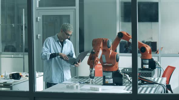 Male Lab Worker is Supervising an Experiment with a Robotic Device alt