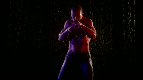 a Muscular Man with a Bare Torso Fights with a Shadow in the Streams of Water on a Dark Background alt