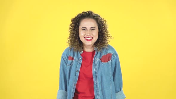 Lovely Curly Girl Smiles Broadly and Winks on Yellow Background at Studio, Slow Motion alt