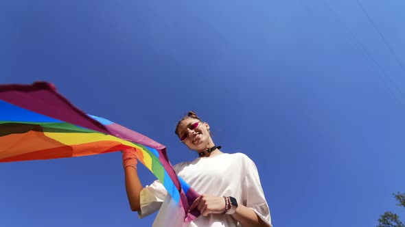 A Young Woman Develops a Rainbow Flag Against the Sky alt