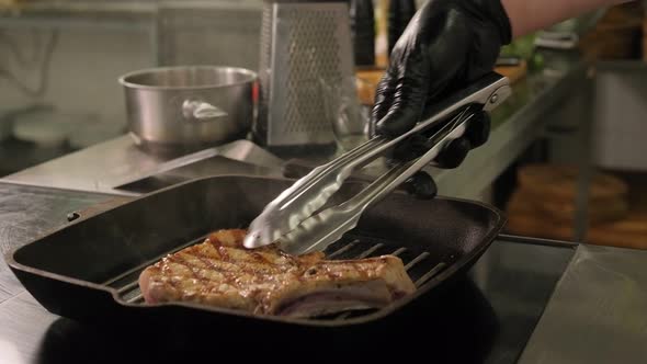 Closeup of a Chef Frying a Pork Steak on a Grill Pan in the Restaurant Kitchen alt