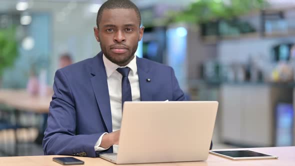 African Businessman with Laptop Doing Thumbs Down in Office alt
