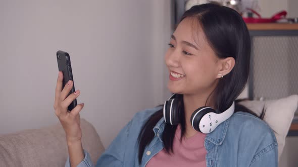 Beautiful young Asian woman having video chat using smartphone While sitting sofa in the living room