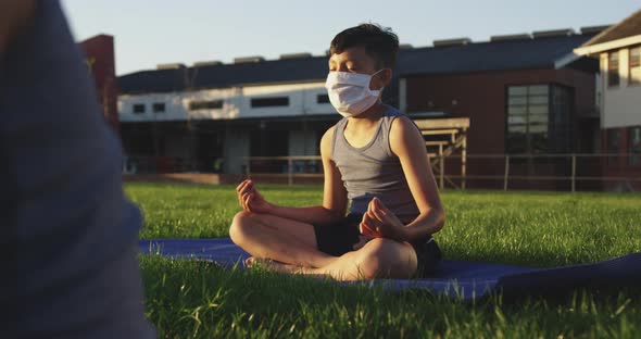 Boy wearing face mask performing yoga in the garden alt
