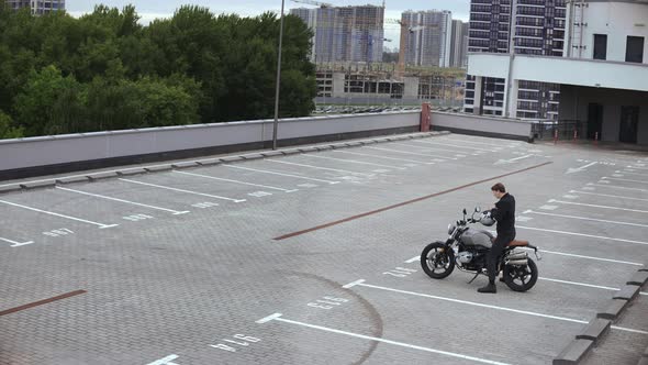 Man Comes to Motorbike and Wears Helmet on Top of the Multilevel Parking alt